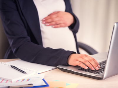 Pregnant woman holding baby bump whilst on the laptop at work 